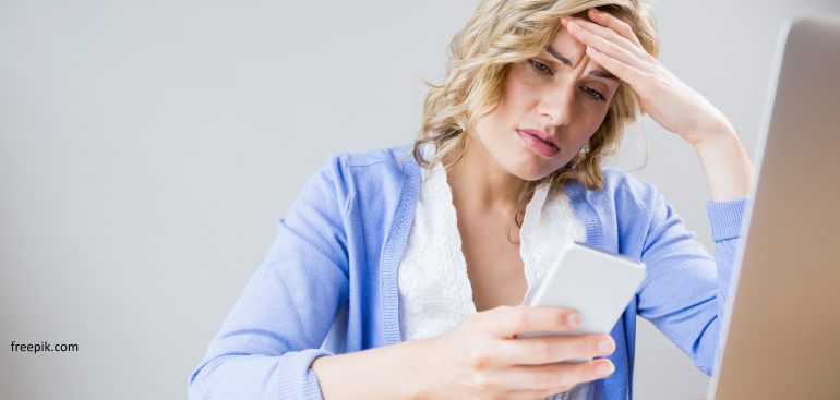 mulher usando celular e computador preocupada